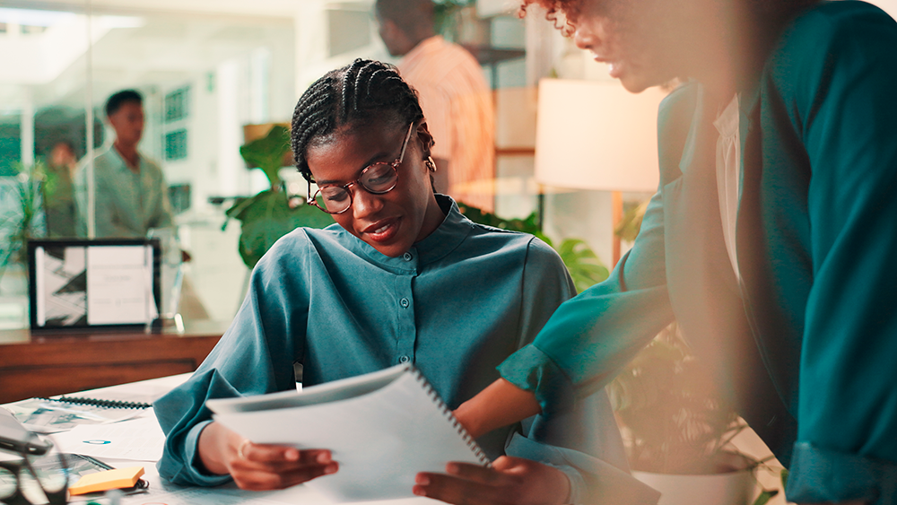 Imagem de duas profissionais planejando juntas como fazer plano de carreira, focadas em traçar metas e construir um plano de carreira sólido. 