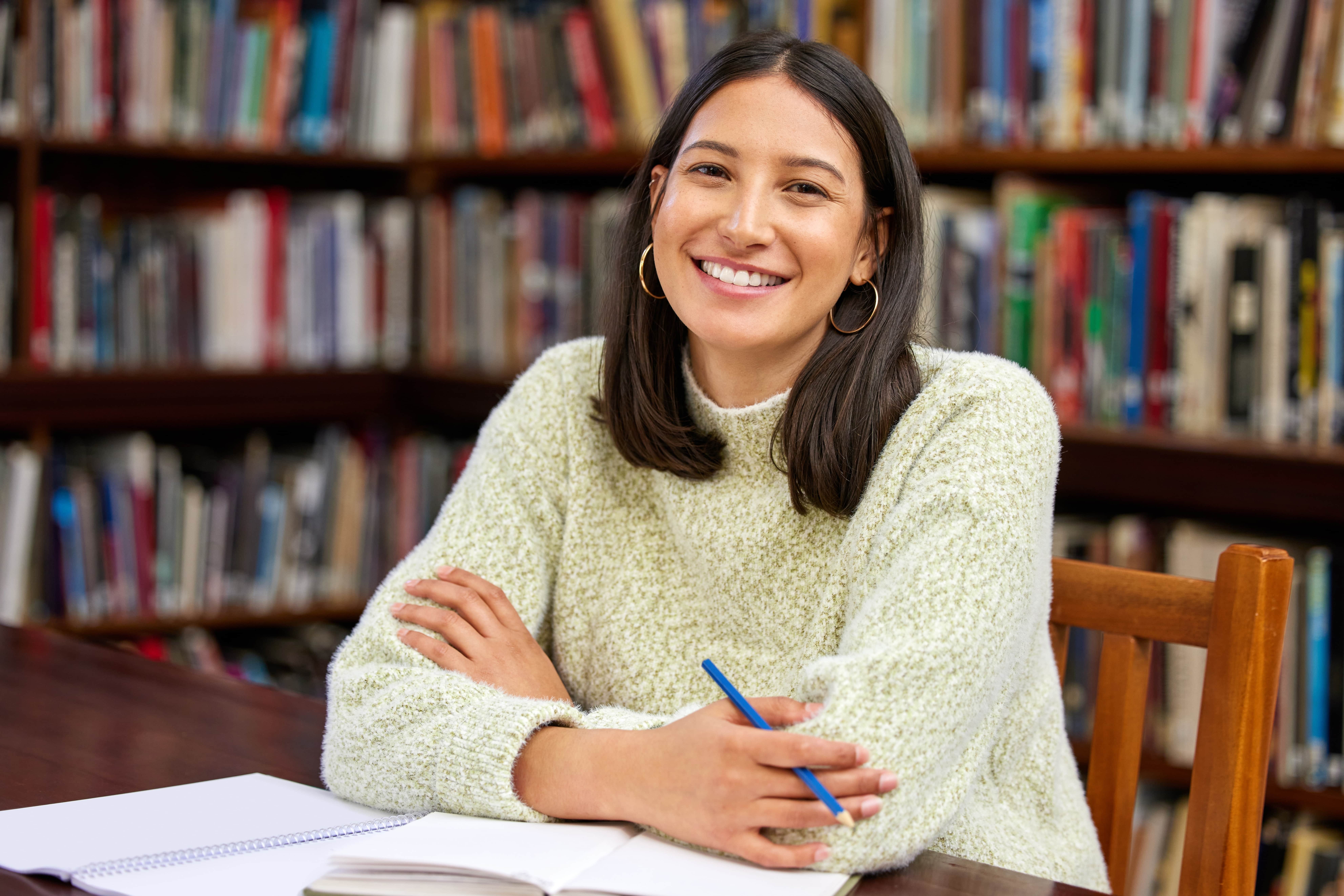 Estudante indígena sorridente em uma biblioteca, simbolizando a presença indígena nas universidades e o avanço no ensino superior.